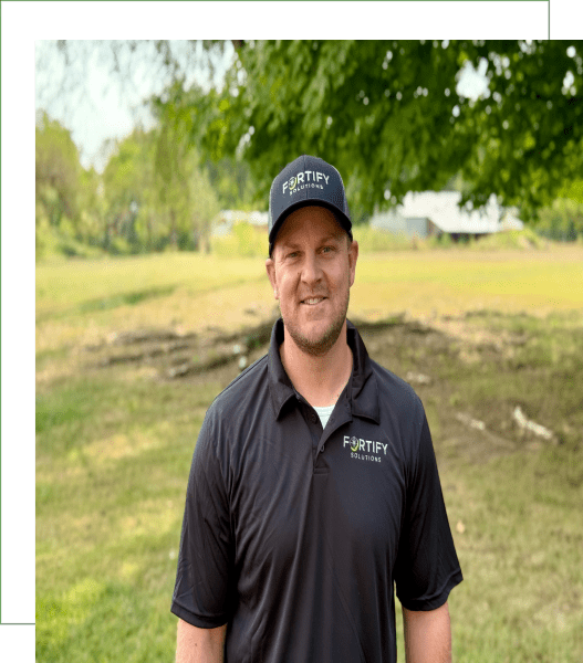 Smiling man outdoors in a black shirt and cap on a sunny day.