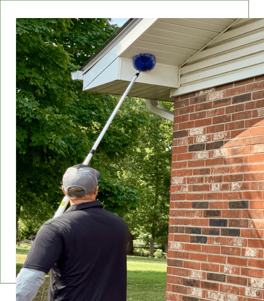Person cleaning house exterior with a long-handled brush.